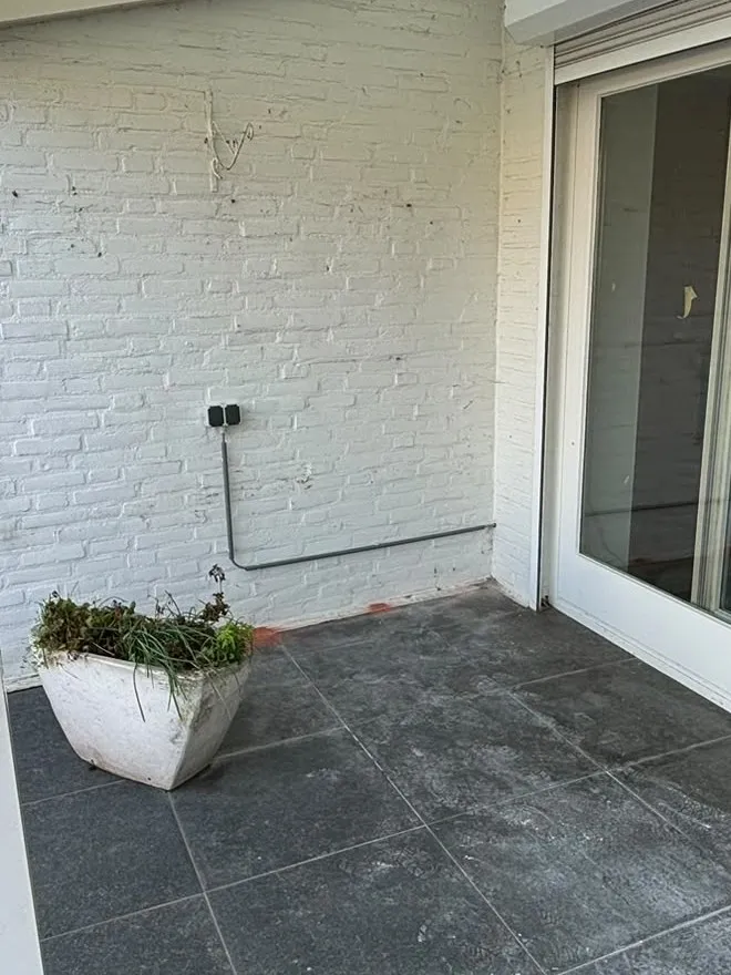 Dubbel buitenstopcontact op een witte muur, met de leiding strak langs de muur