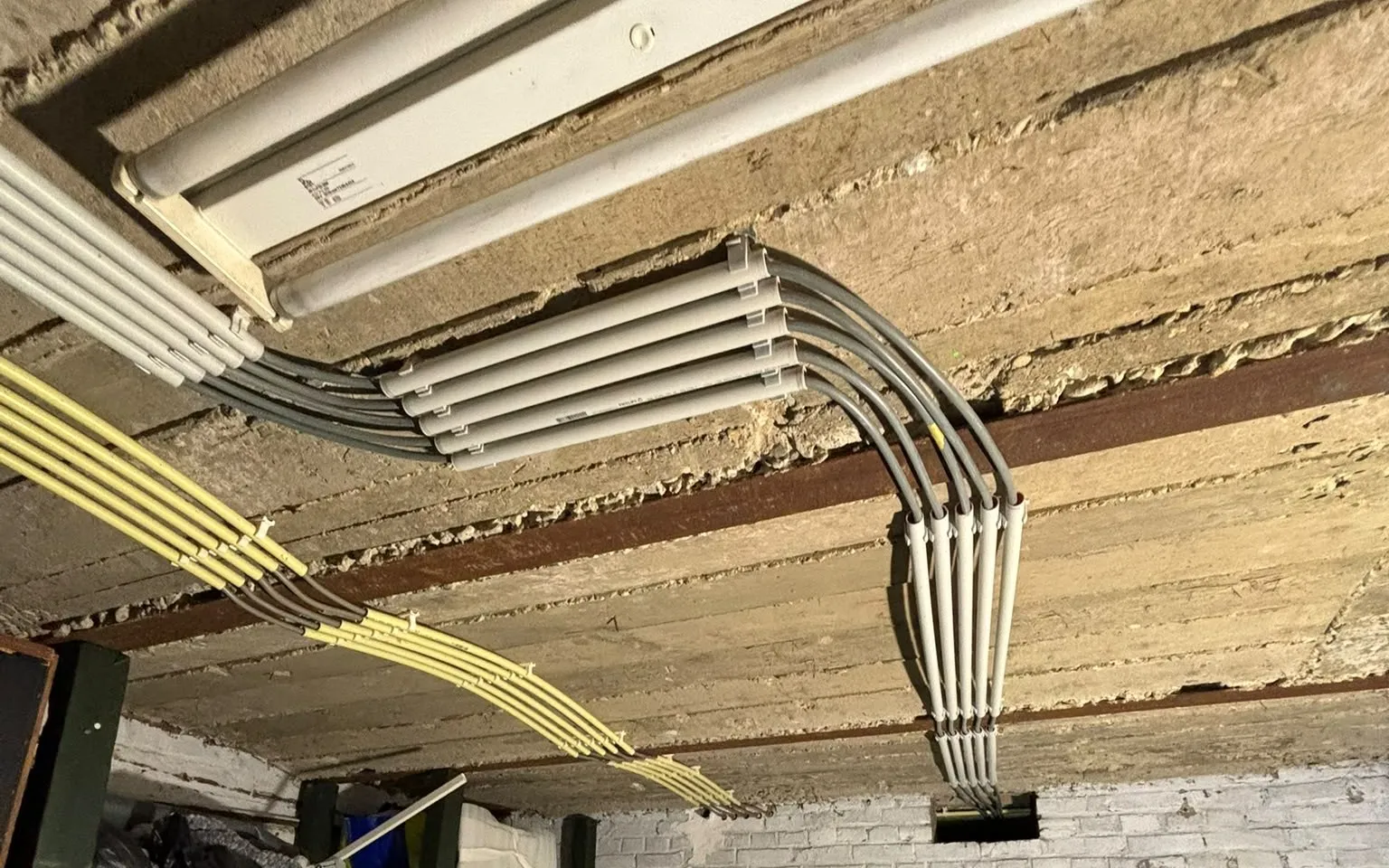 Gebundelde leidingen tegen een kelderplafond, met gelijke bochten naast elkaar